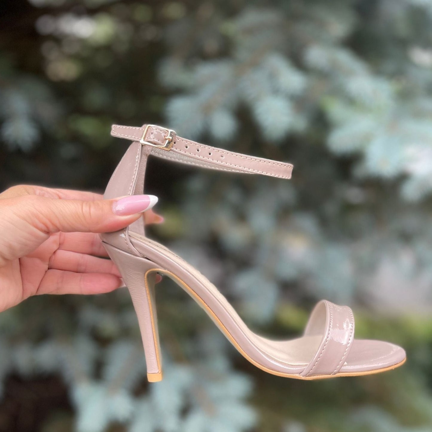 A woman holding a pair of nude strappy heels