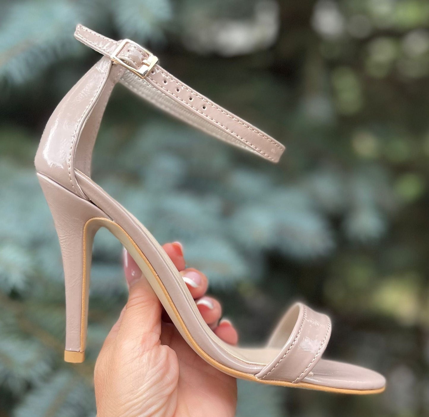 A woman holding a pair of nude strappy heels