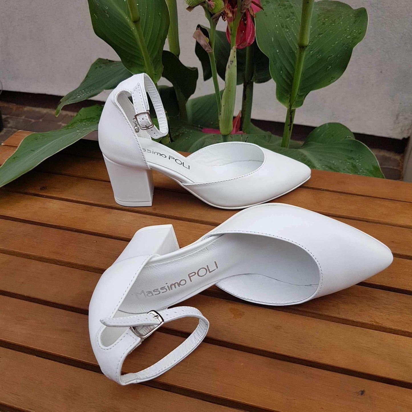 White leather heels on a wooden table surrounded by flowers