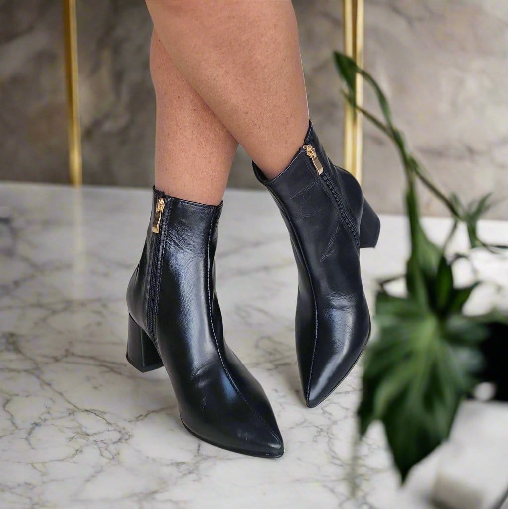 Woman wearing black ankle boots with a gold zip and a block heel