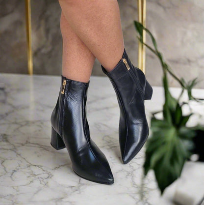 Woman wearing black ankle boots with a gold zip and a block heel